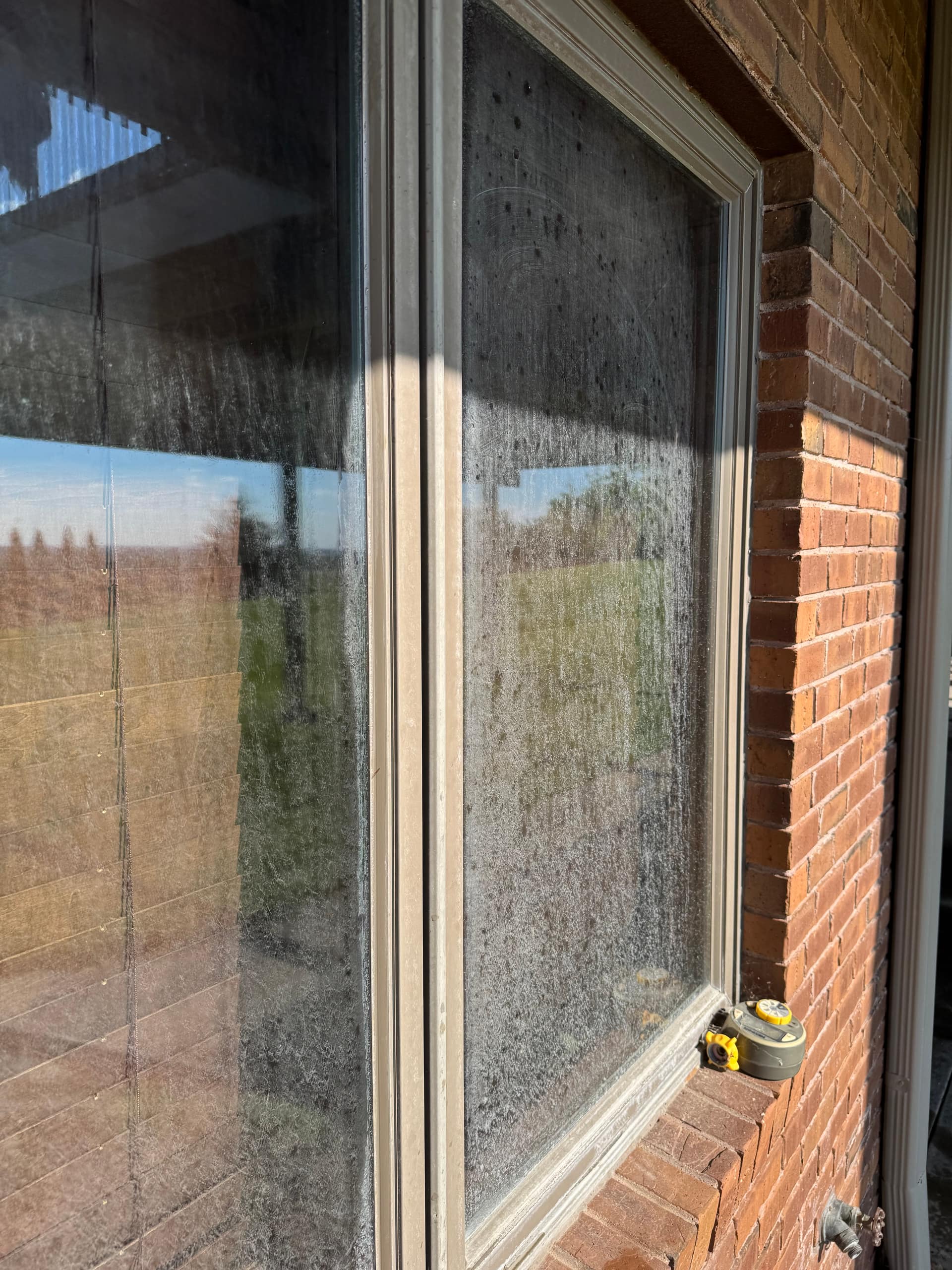 Before/after composite on a single Omaha window — sprinkler-fed bonded mineral spotting on top, the same glass restored to clear on the bottom